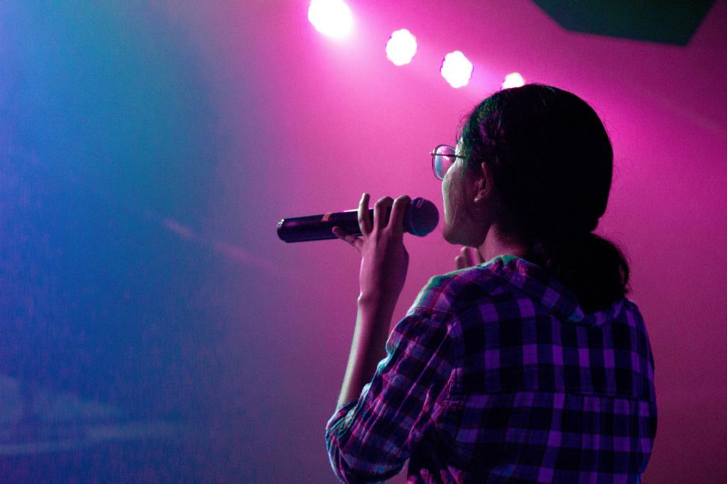 Woman singing on stage and colored lights of purple, blue and pink.