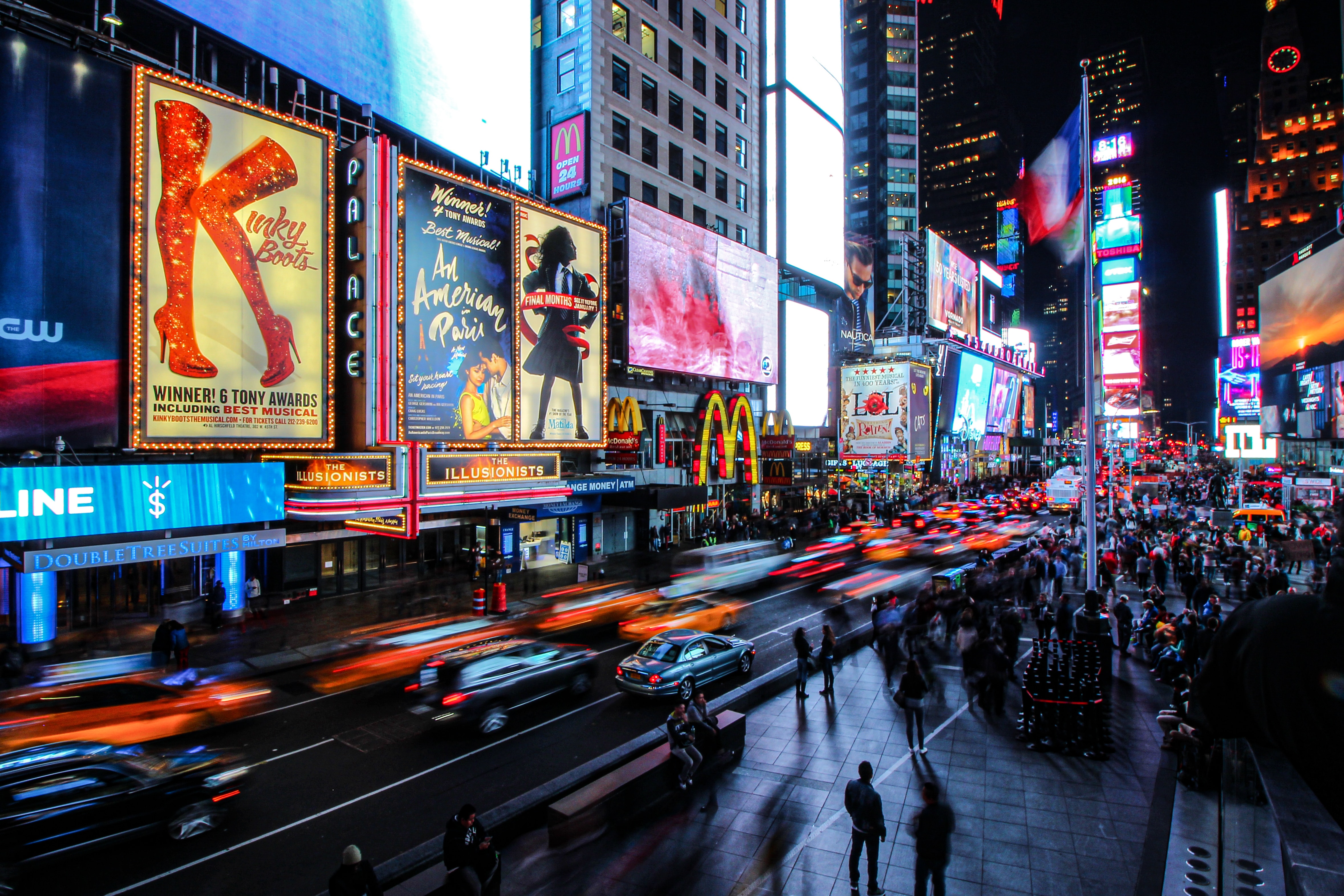 New York City showing large screens of musicals, advertisements, people and cars at night.