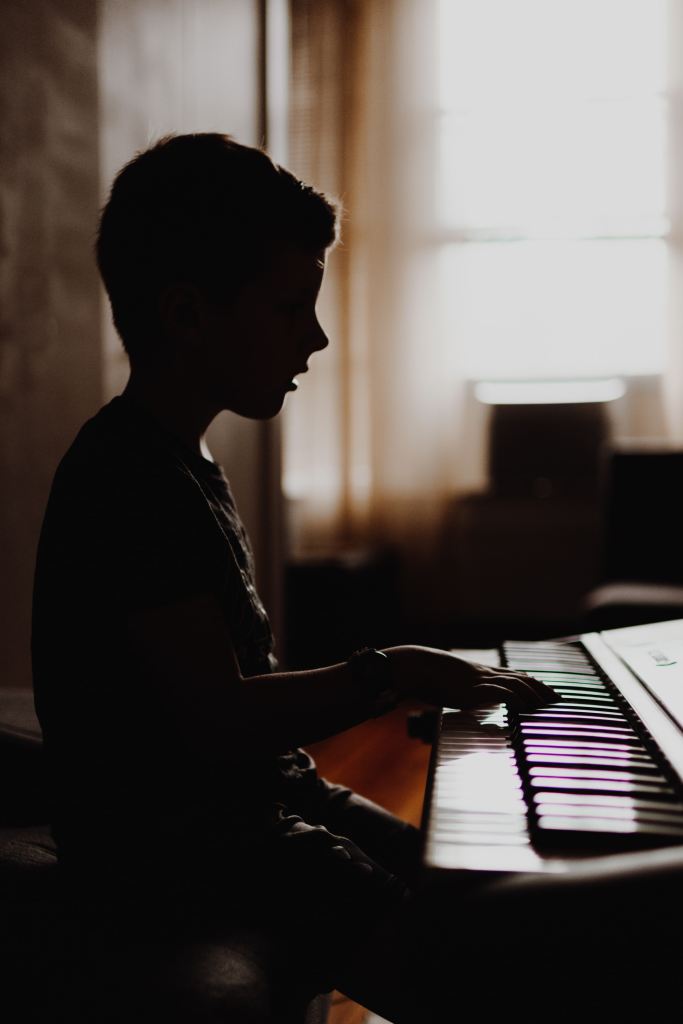 Child playing piano keyboard in a shadow lighting pattern from a side angle